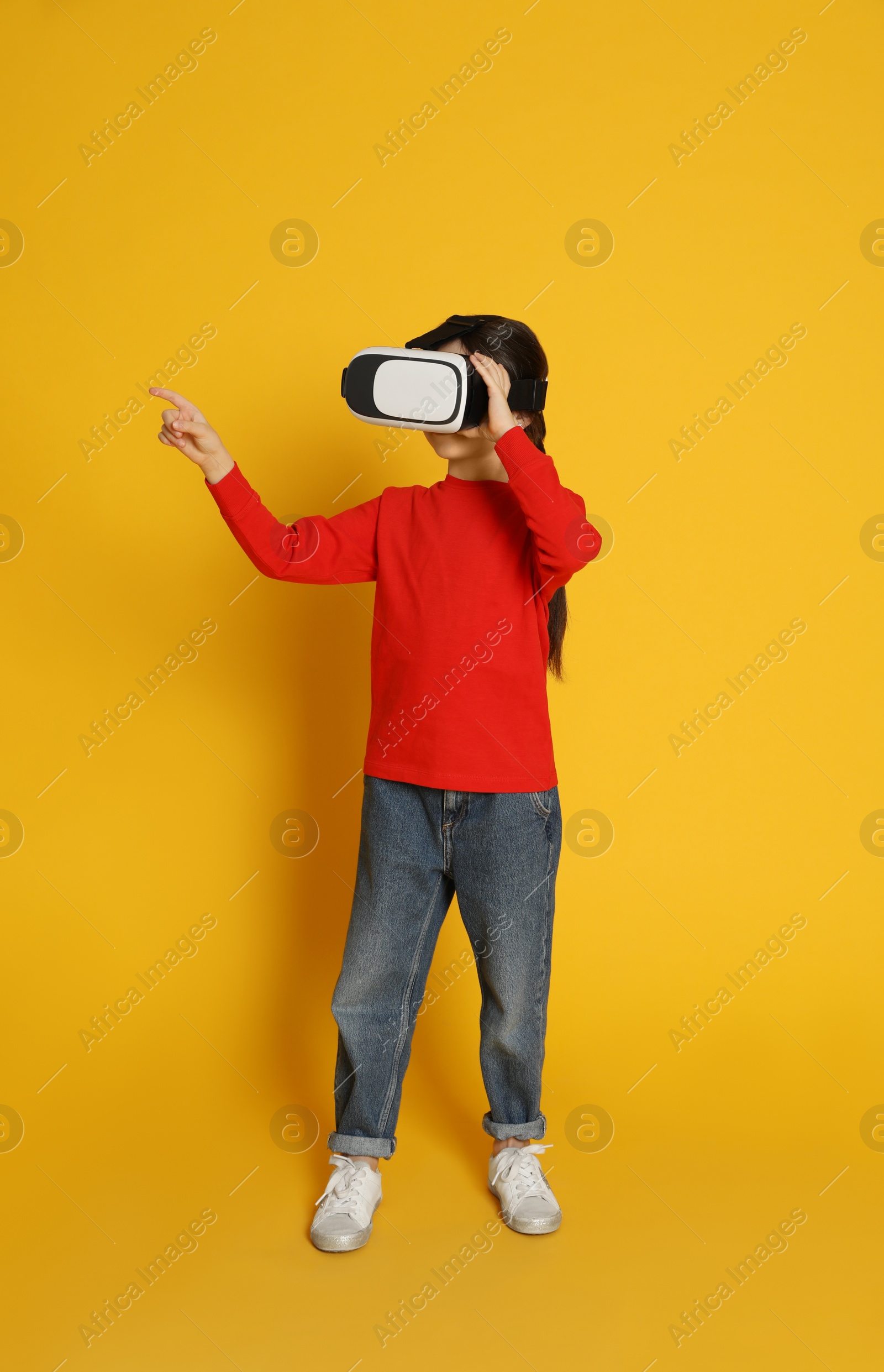 Photo of Little girl using virtual reality headset on yellow background