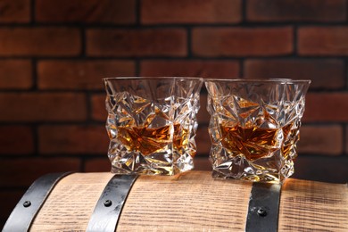 Photo of Glasses of whiskey on wooden barrel against brick wall, closeup