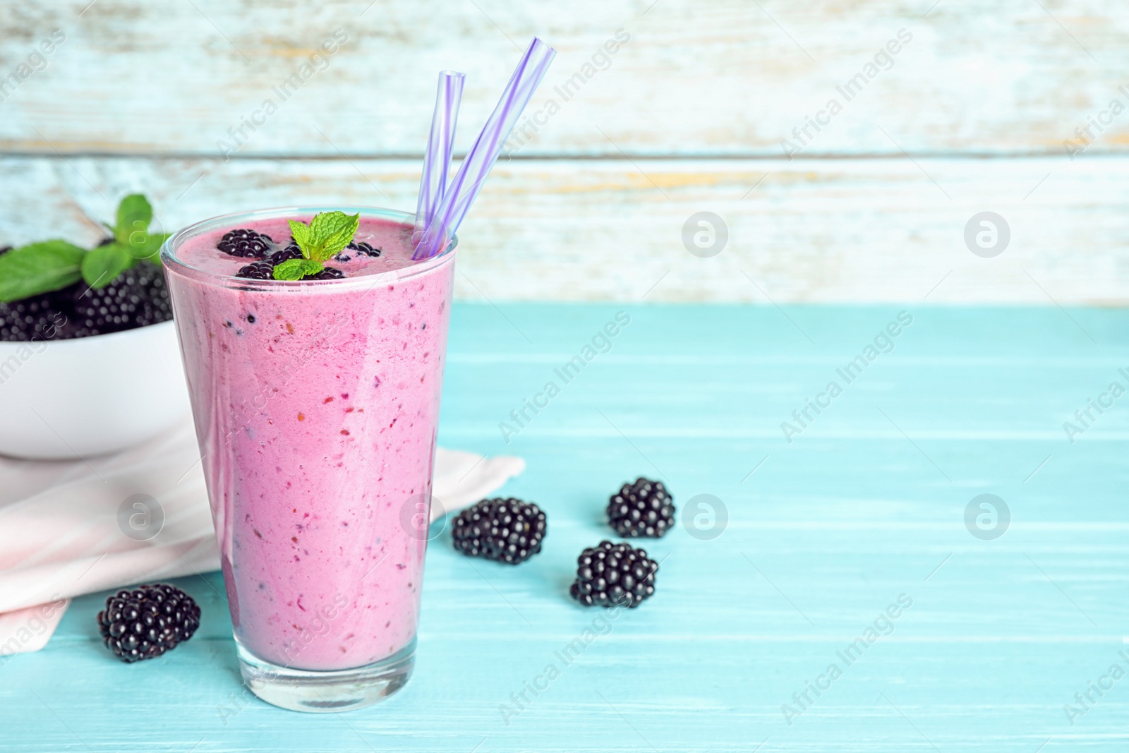 Photo of Delicious blackberry smoothie in glass on light blue wooden table. Space for text