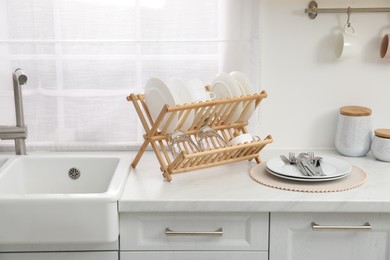 Drying rack with clean dishes on light marble countertop near sink in kitchen