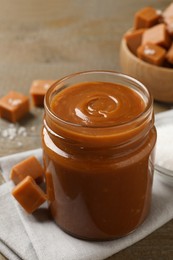 Photo of Yummy salted caramel in glass jar and candies on wooden table