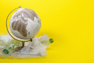 Photo of Globe in plastic bag and garbage on yellow background, space for text. Environmental conservation