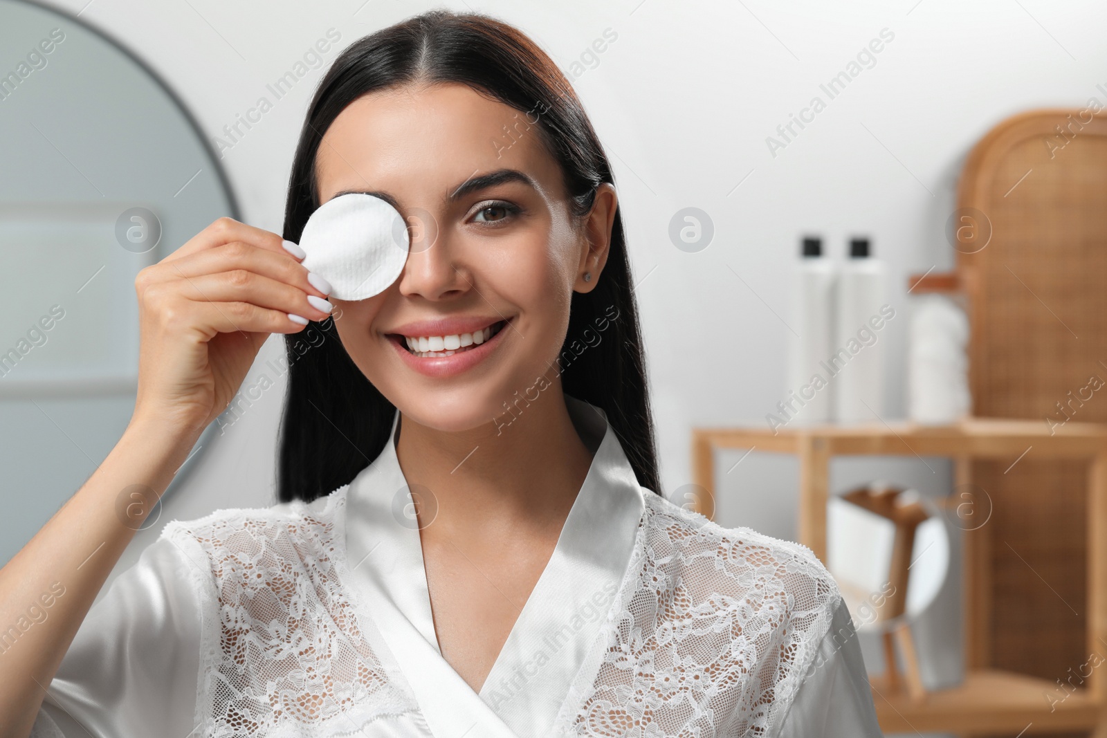 Photo of Young woman using cotton pad with micellar water indoors