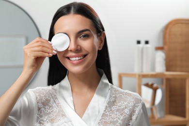 Young woman using cotton pad with micellar water indoors