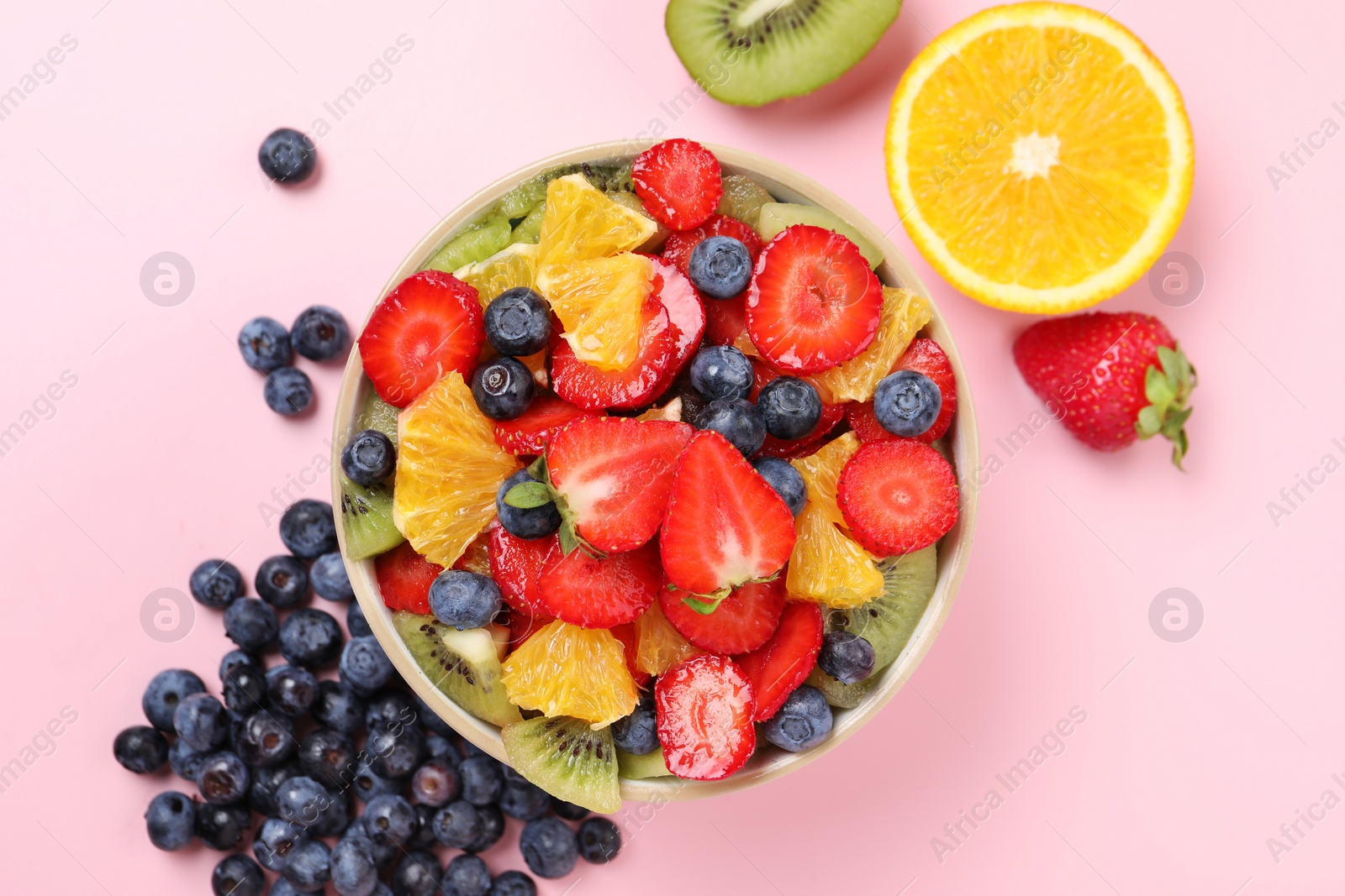 Photo of Yummy fruit salad in bowl and ingredients on pink background, flat lay