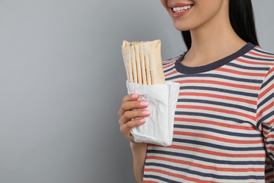 Young woman with delicious shawarma on grey background, closeup. Space for text