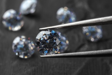 Tweezers with beautiful shiny diamond above dark gray table, closeup