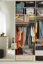 Photo of Wardrobe closet with different stylish clothes and home stuff in room. Fast fashion