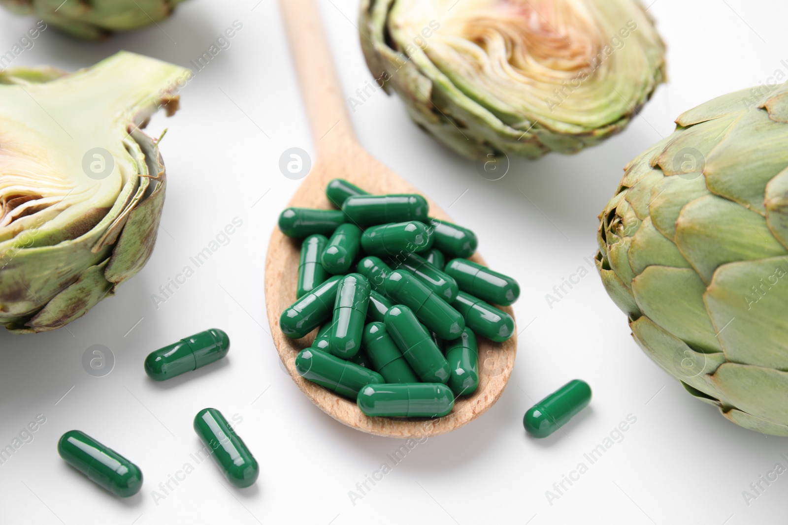 Photo of Spoon with pills and fresh artichokes on white background, closeup