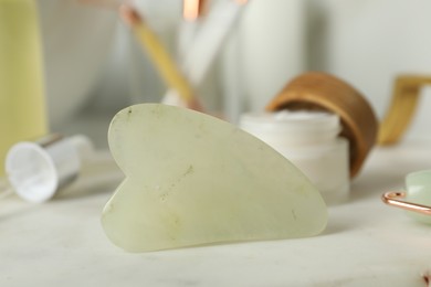 Jade gua sha tool and toiletries on white table, closeup