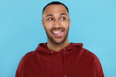 Photo of Happy young man showing his tongue on light blue background