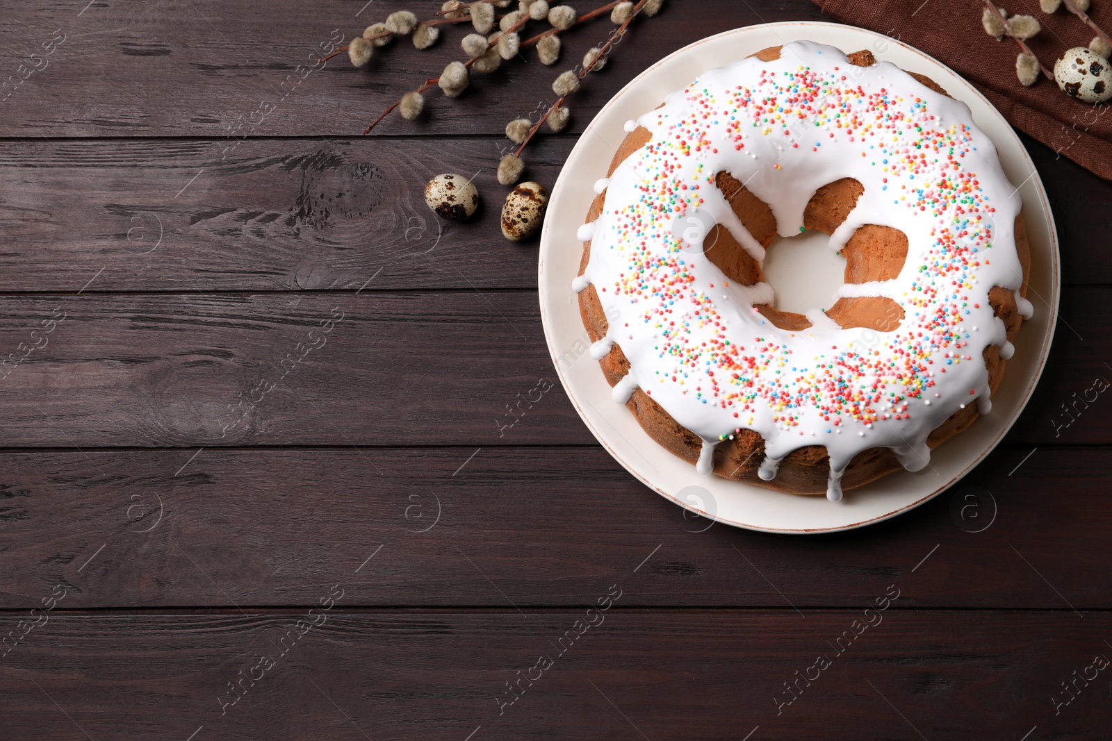 Photo of Glazed Easter cake with sprinkles, quail eggs and willow branches on wooden table, flat lay. Space for text