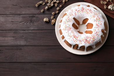 Glazed Easter cake with sprinkles, quail eggs and willow branches on wooden table, flat lay. Space for text