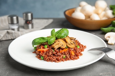 Photo of Plate of tasty brown rice with vegetables and mushrooms on grey table