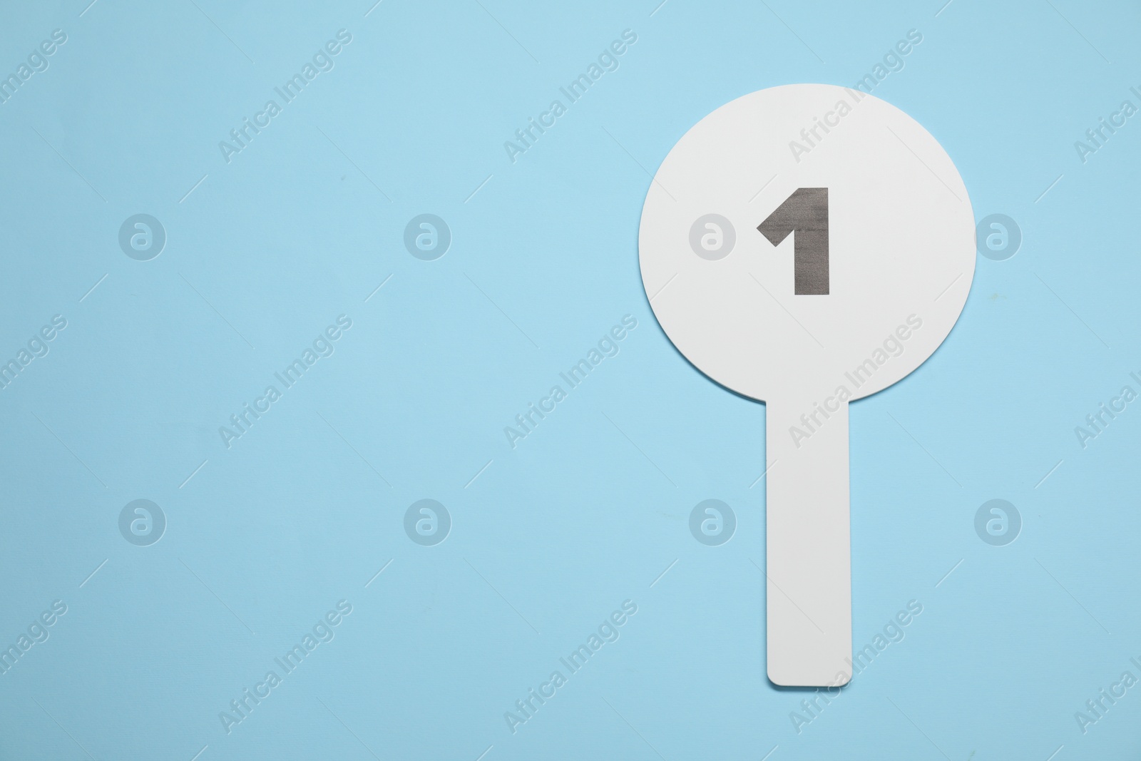 Photo of Auction paddle with number 1 on light blue background, top view. Space for text