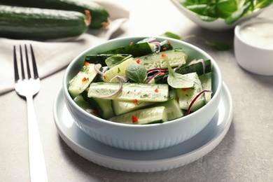 Photo of Delicious cucumber salad with onion and spinach in bowl served on table