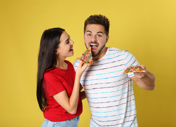 Young couple with pizza on yellow background