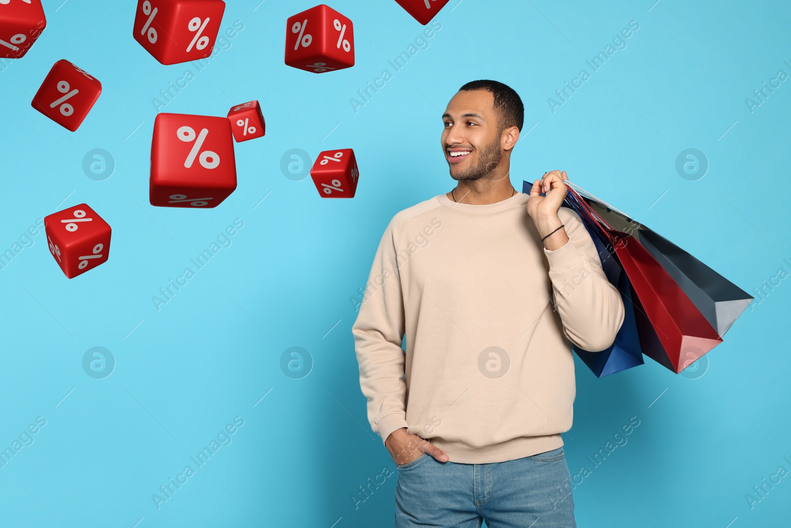 Image of Discount offer. Happy man with paper shopping bags looking at falling cubes with percent signs on light blue background