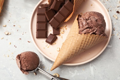 Photo of Delicious ice cream in wafer cone and chocolate pieces on light grey table, flat lay