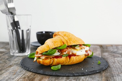 Photo of Tasty croissant sandwich with bacon on wooden table