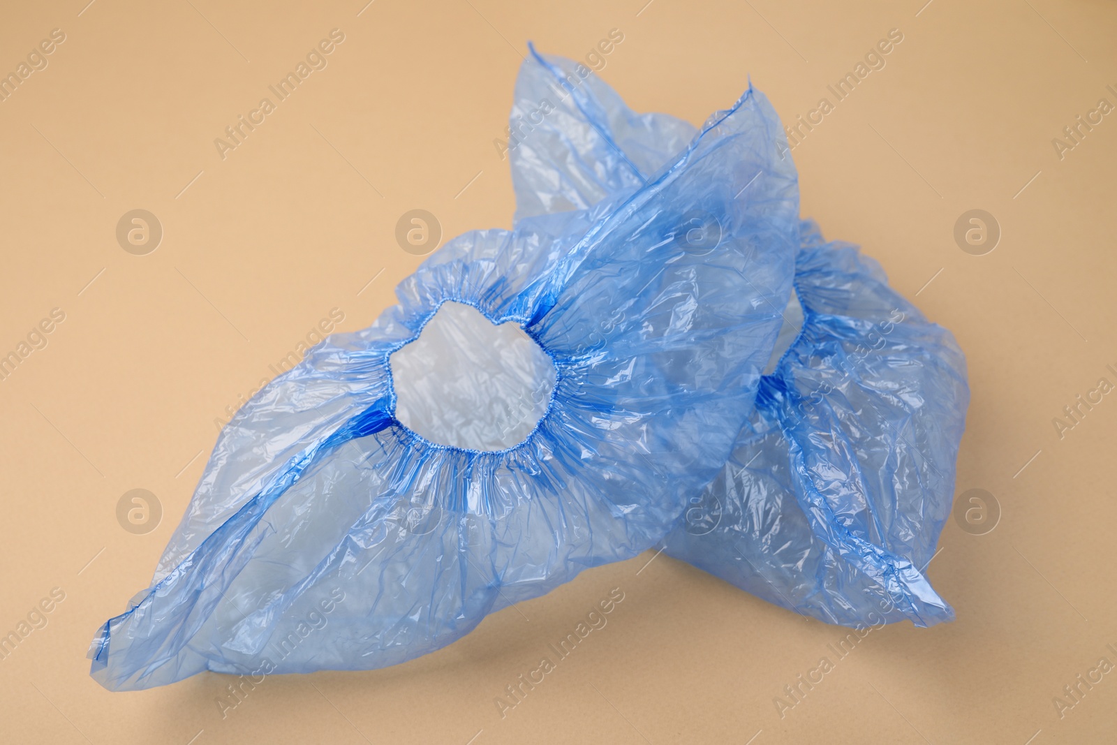 Photo of Pair of blue medical shoe covers on beige background, closeup