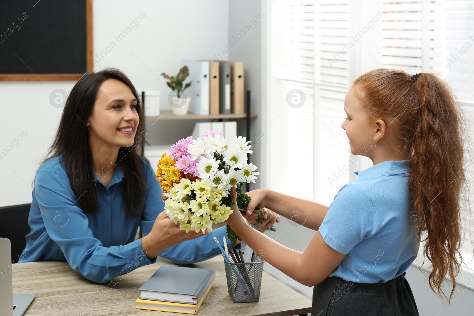 Photo of Schoolgirl congratulating her pedagogue with bouquet in classroom. Teacher's day