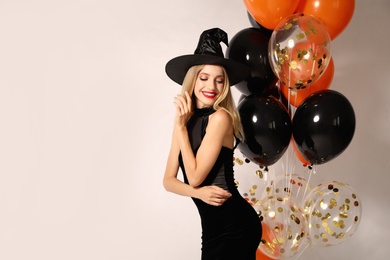 Photo of Beautiful woman in witch costume with balloons on white background, space for text. Halloween party