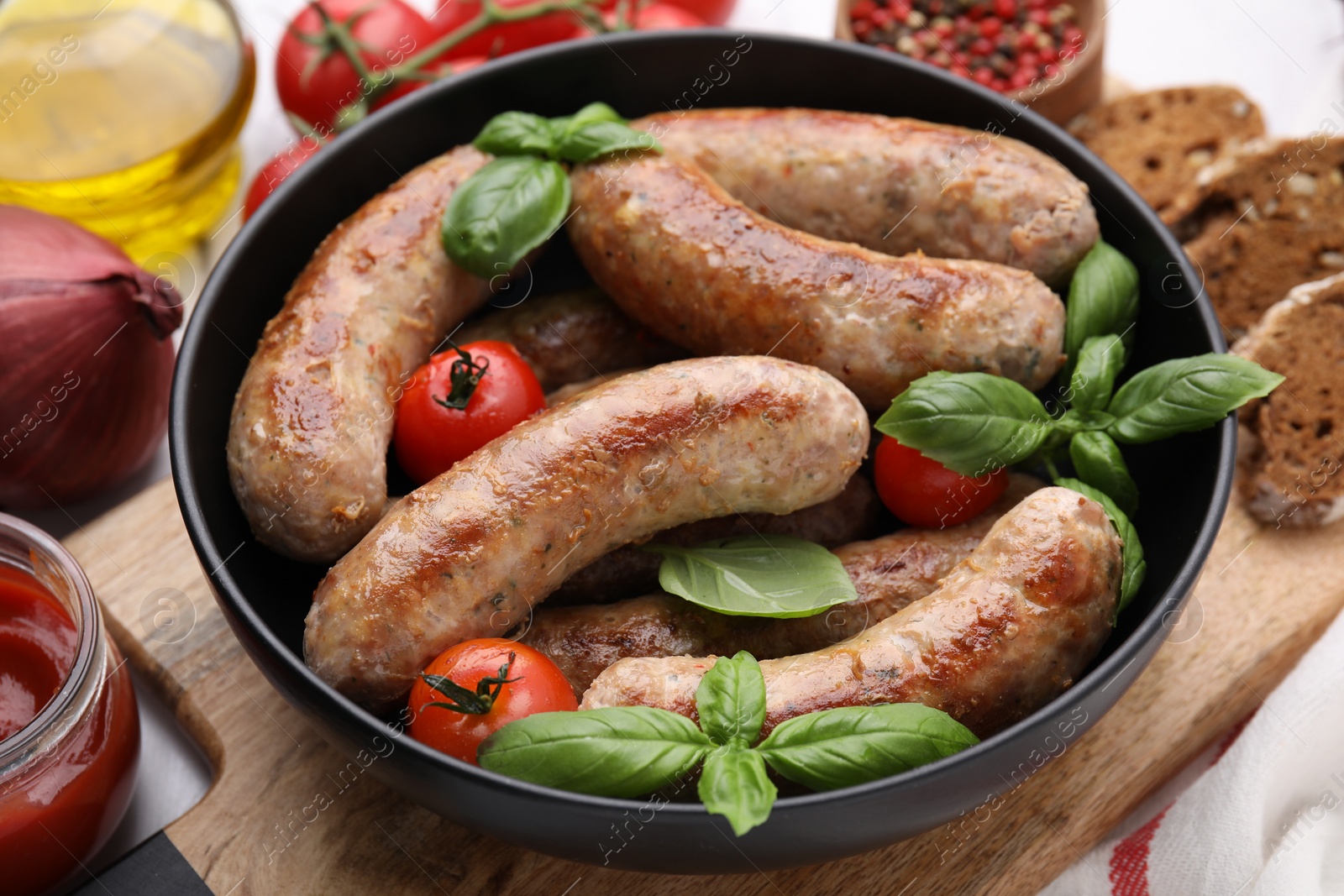 Photo of Bowl with tasty homemade sausages, basil leaves and tomatoes on table, closeup