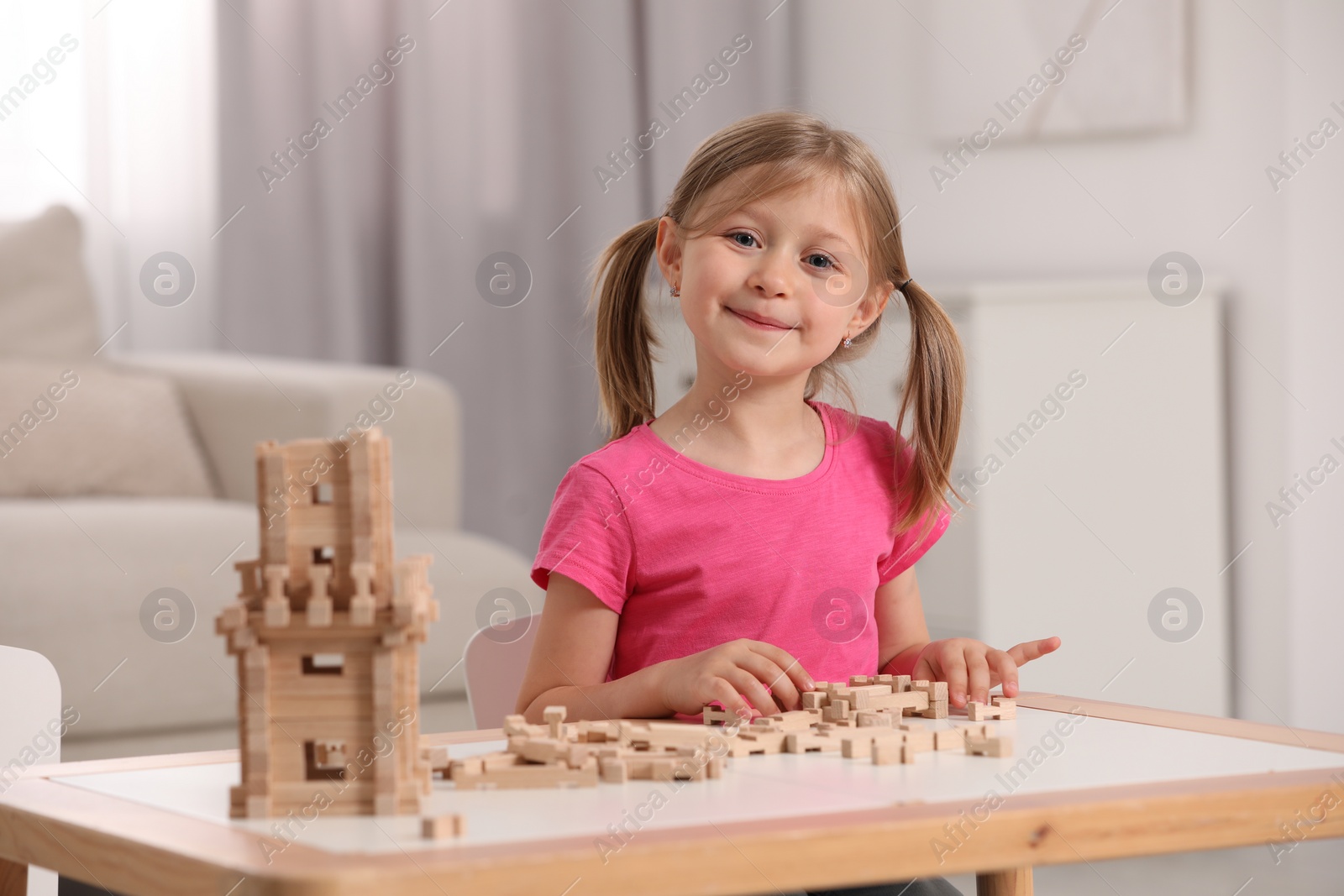 Photo of Cute little girl playing with wooden tower at table indoors. Child's toy