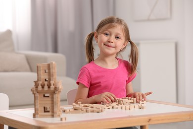 Cute little girl playing with wooden tower at table indoors. Child's toy