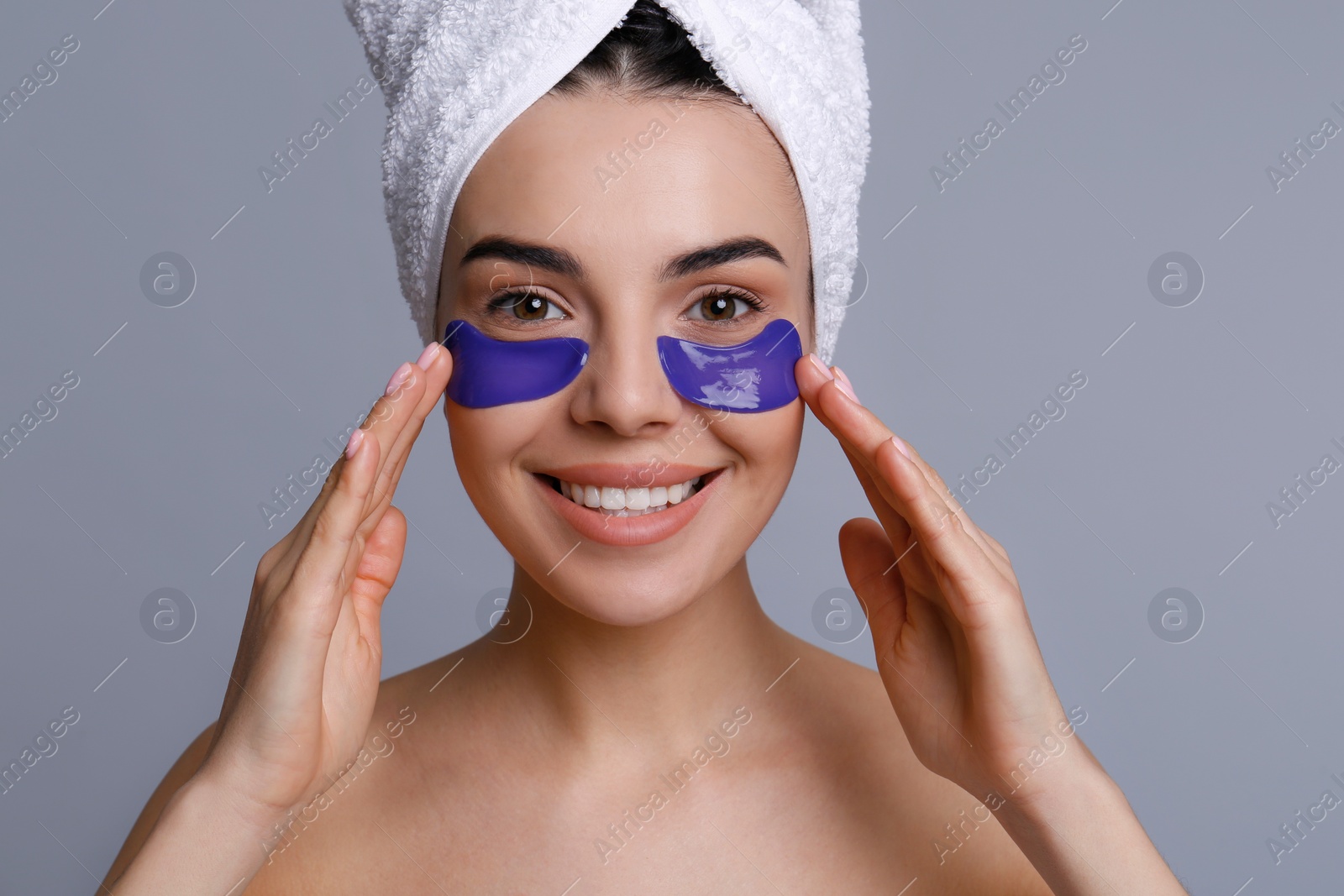 Photo of Beautiful young woman with under eye patches and hair wrapped in towel on grey background