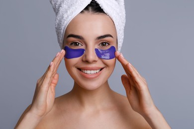 Beautiful young woman with under eye patches and hair wrapped in towel on grey background