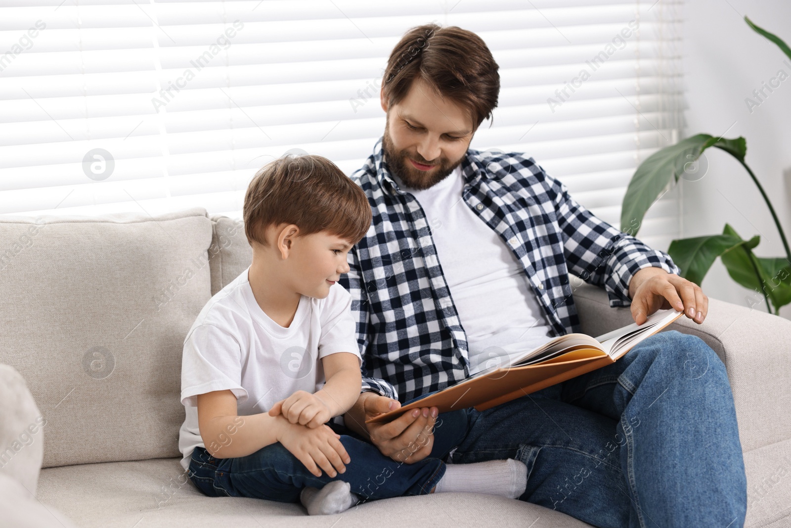 Photo of Dad and son reading book together on sofa at home