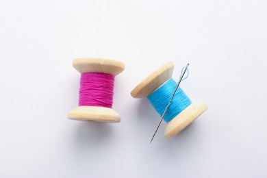 Colorful sewing threads with needle on white background, top view