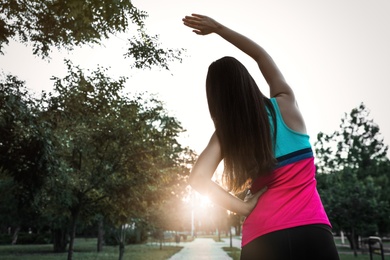 Photo of Young woman stretching before morning run in park, back view. Space for text