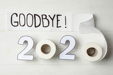 Photo of Text Goodbye 2020 and toilet paper on white wooden background, flat lay