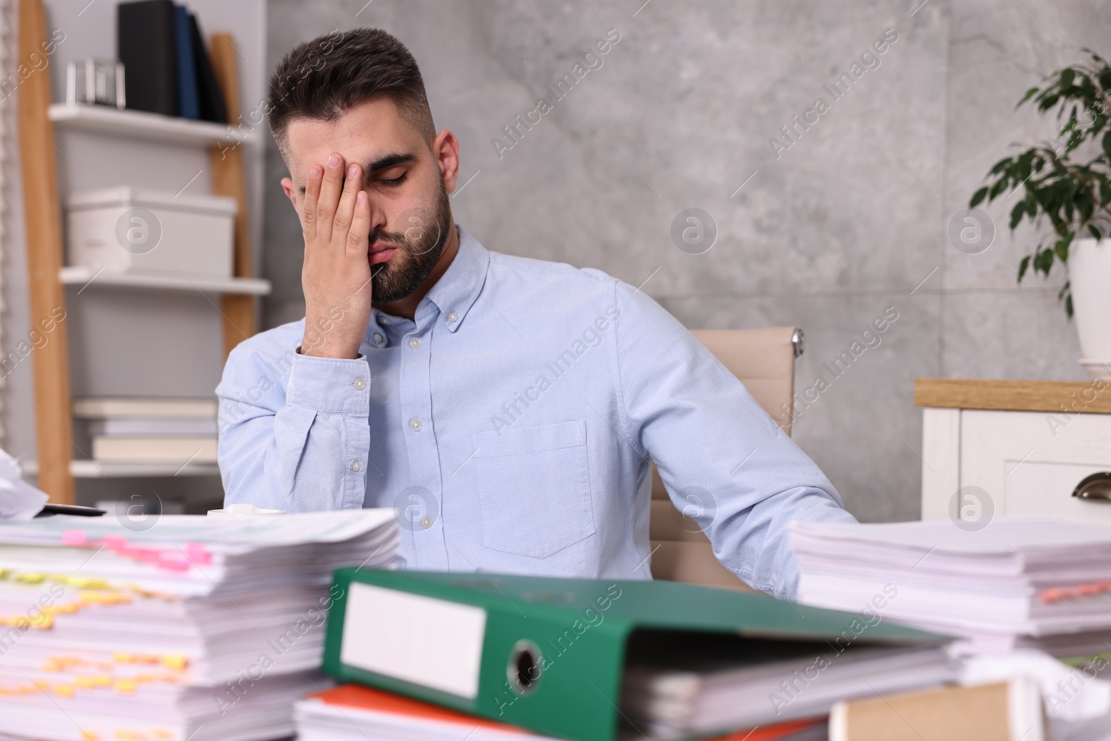 Photo of Overwhelmed man surrounded by documents at workplace in office