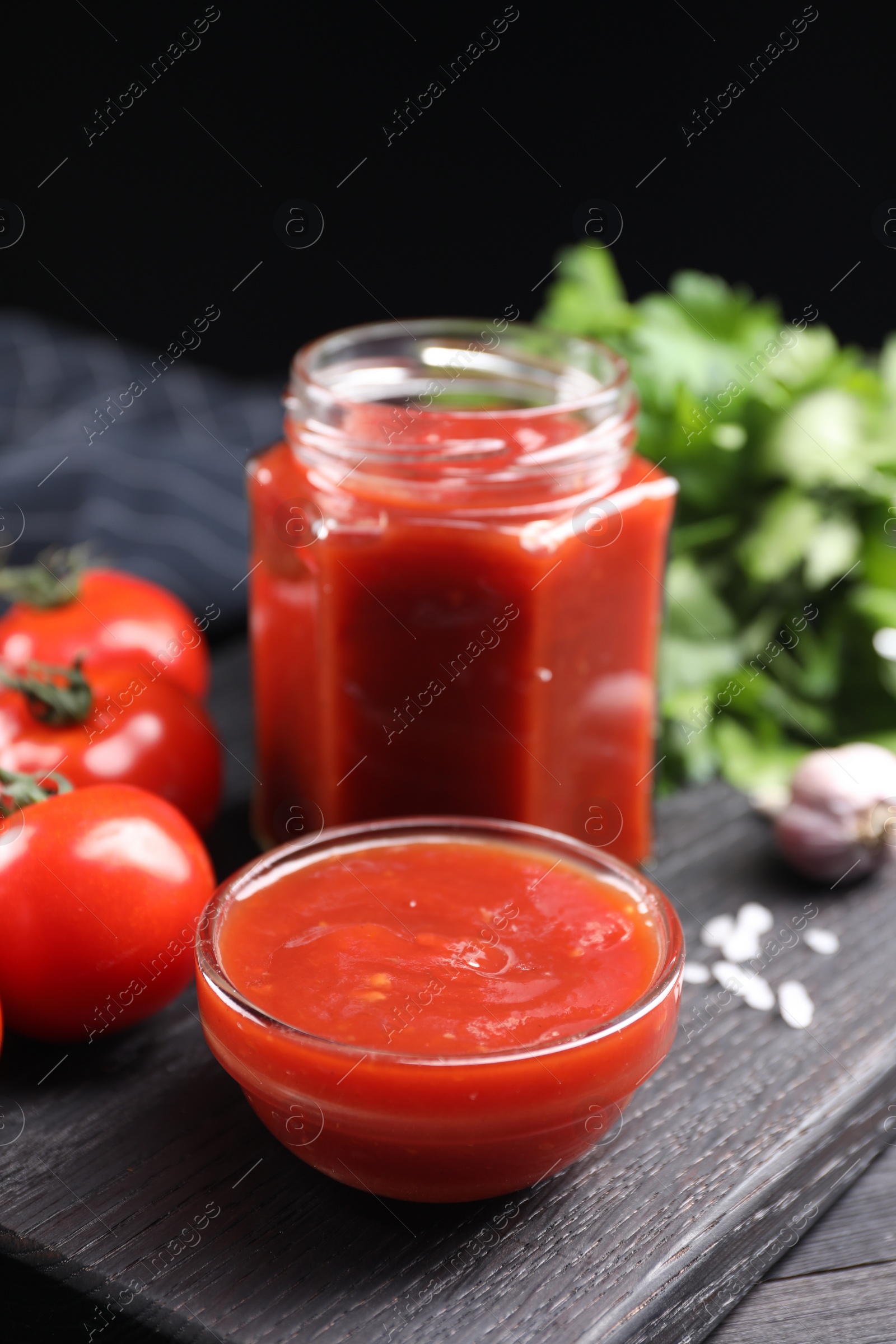 Photo of Delicious ketchup on black wooden table, closeup. Tomato sauce