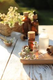 Photo of Chamomile essential oil, pipette and flowers on white wooden table outdoors