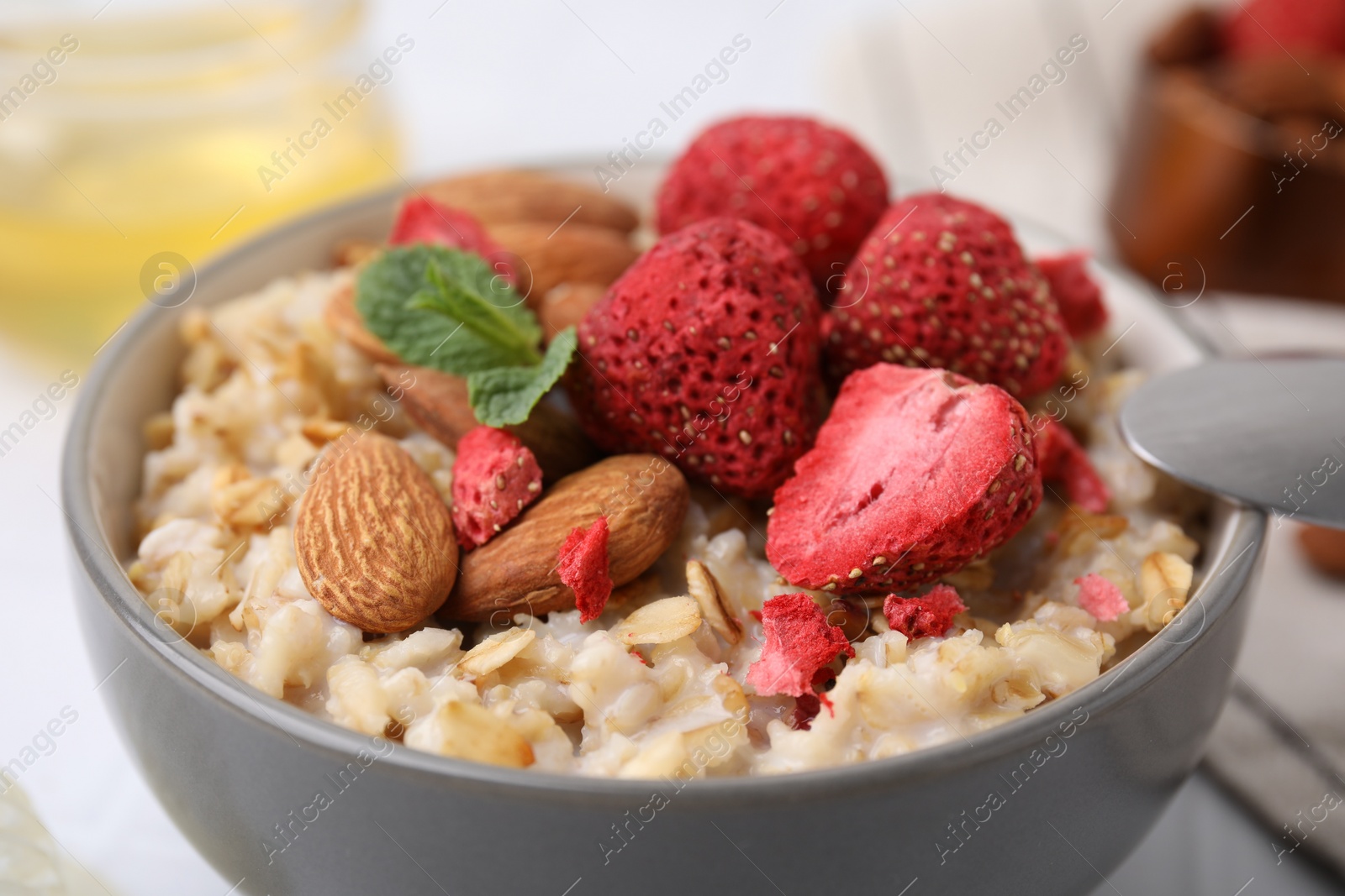 Photo of Delicious oatmeal with freeze dried strawberries, almonds and mint in bowl, closeup