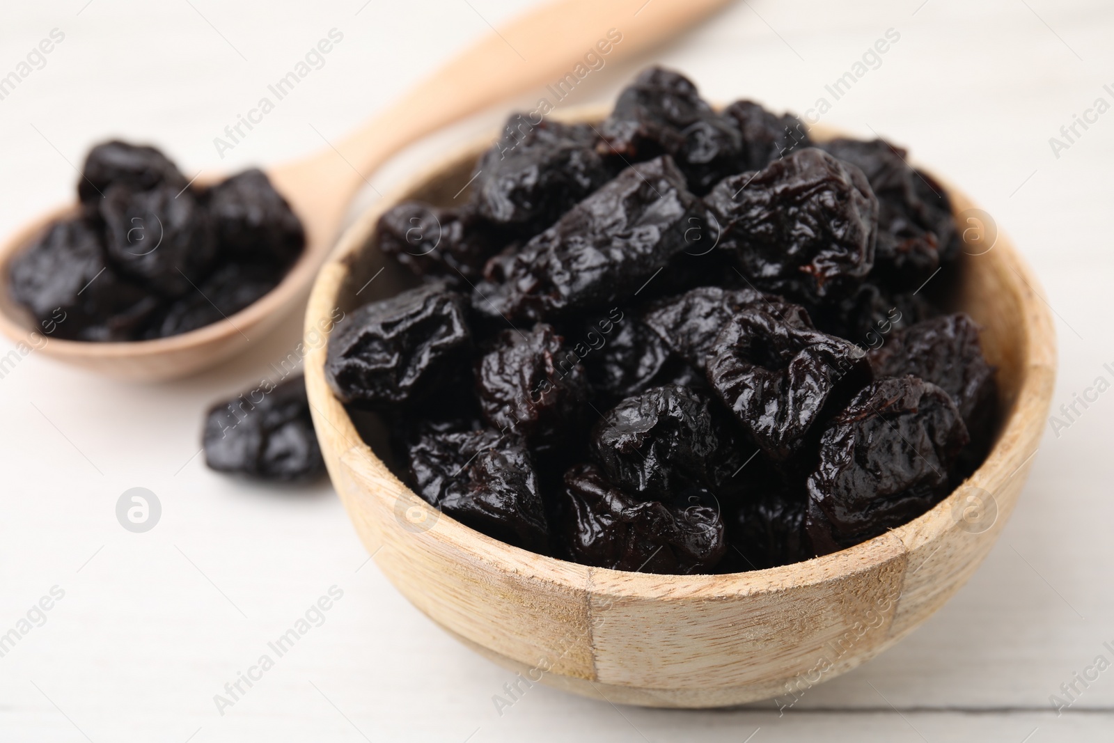 Photo of Bowl and spoon with sweet dried prunes on white table, closeup