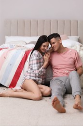 Happy couple resting on floor near bed after pillow fight
