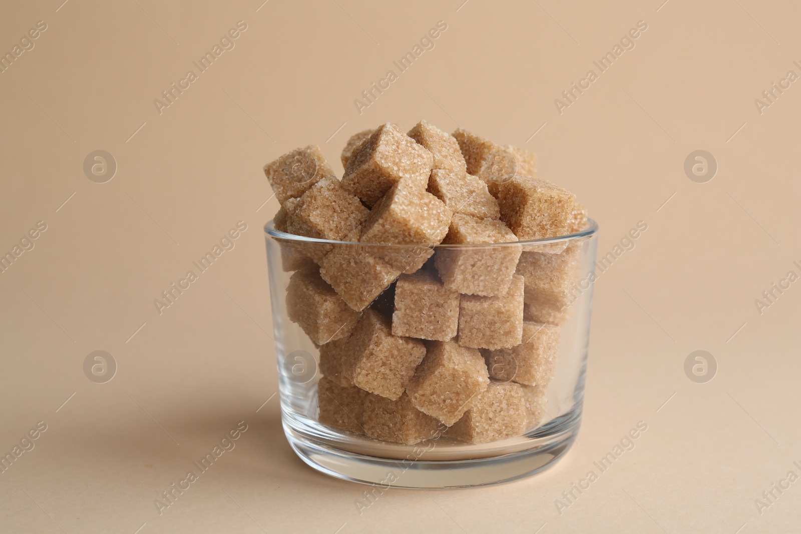 Photo of Brown sugar cubes in glass on beige background, closeup