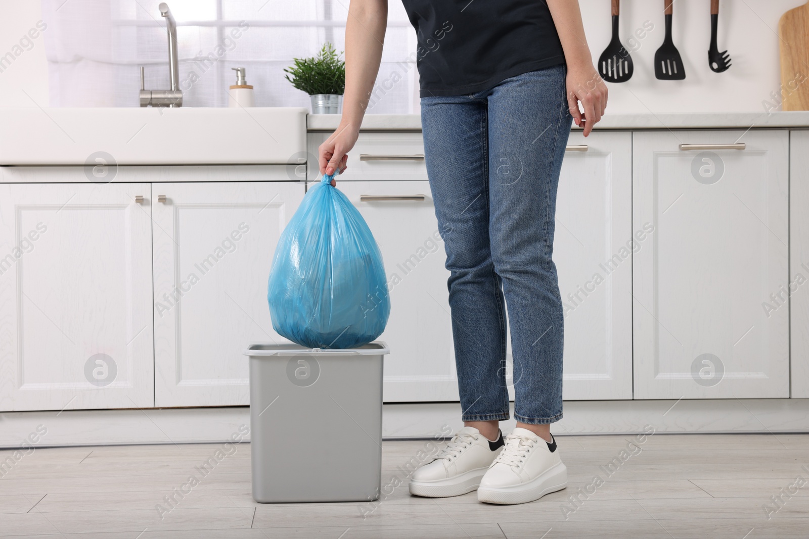 Photo of Woman taking garbage bag out of trash bin in kitchen, closeup