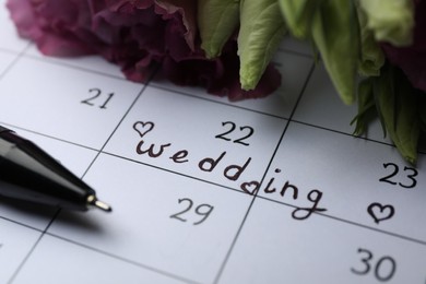 Calendar with date reminder about Wedding Day, pen and flowers, closeup