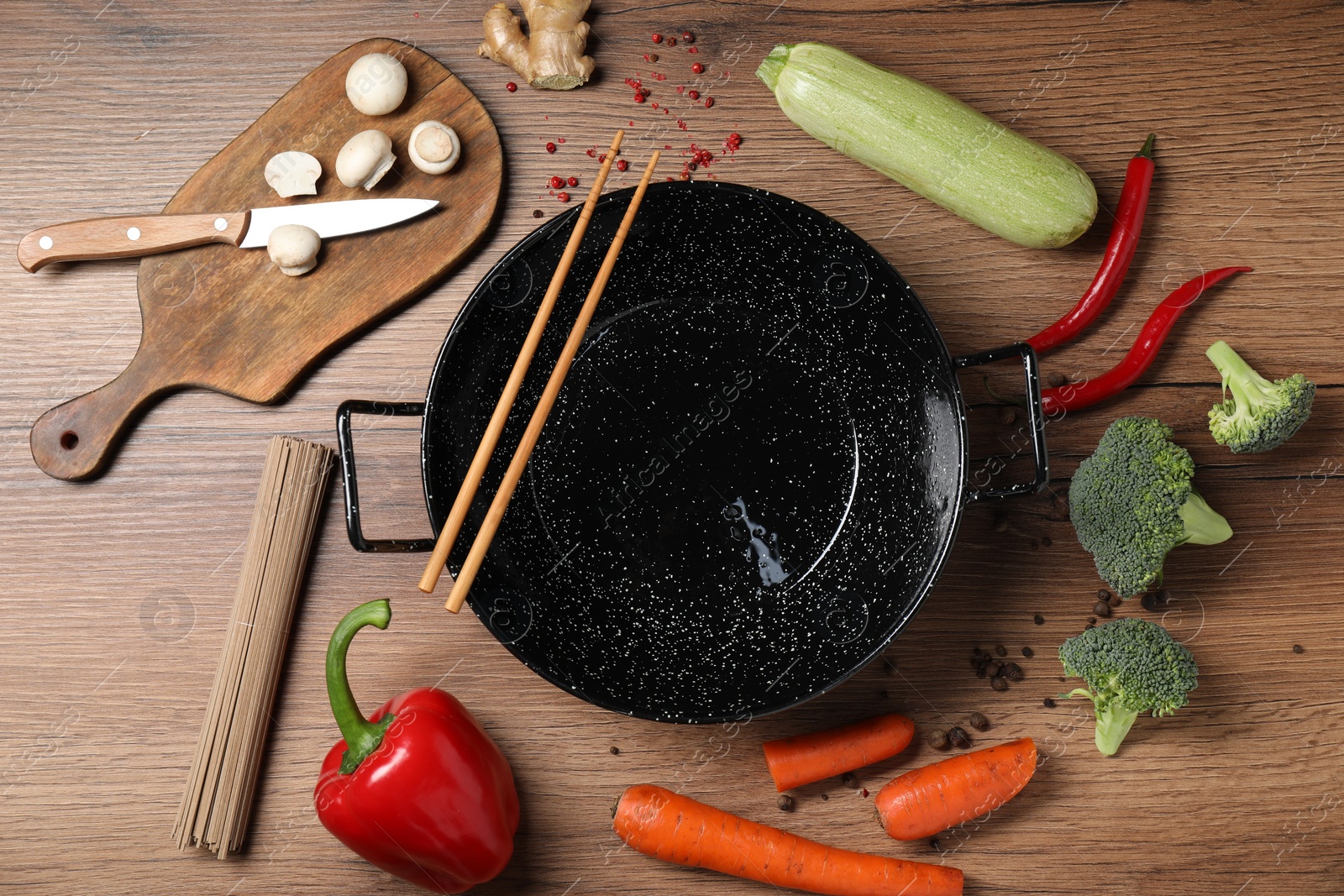 Photo of Empty iron wok surrounded by raw ingredients on wooden table, flat lay