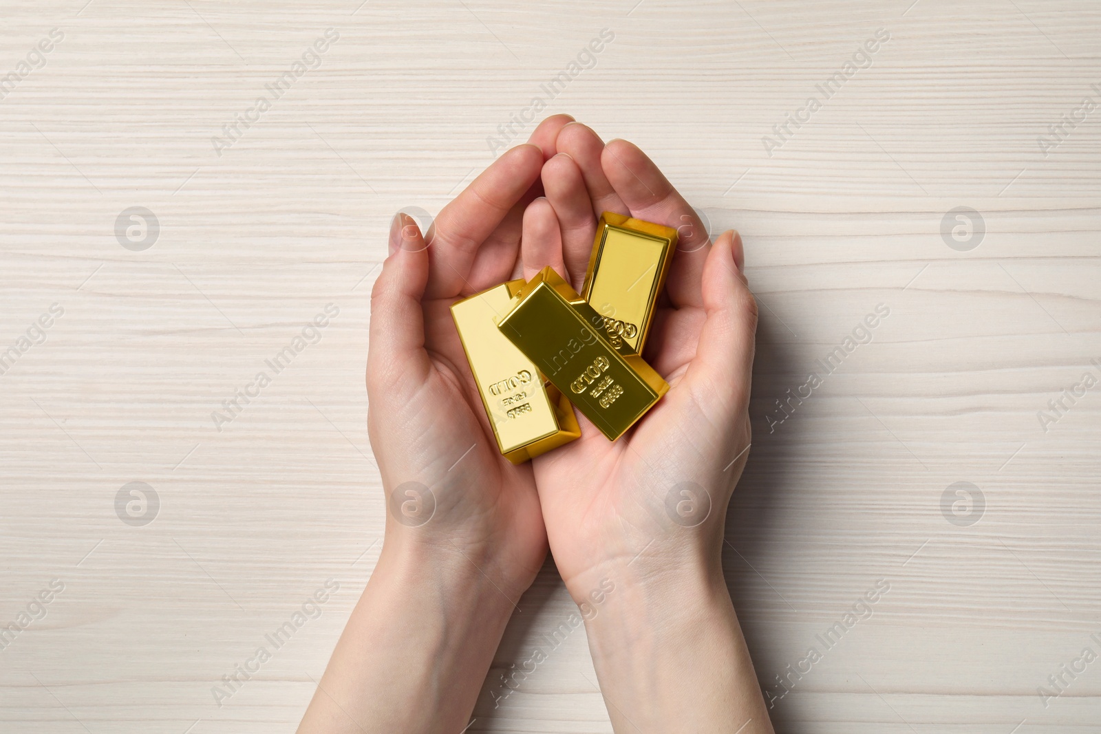 Photo of Woman holding gold bars on white wooden table, top view