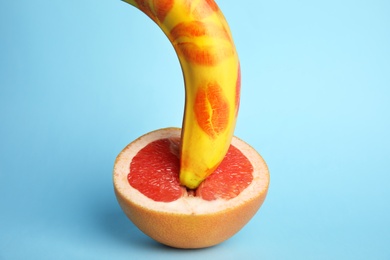 Photo of Fresh banana with red lipstick marks and grapefruit on blue background. Sex concept