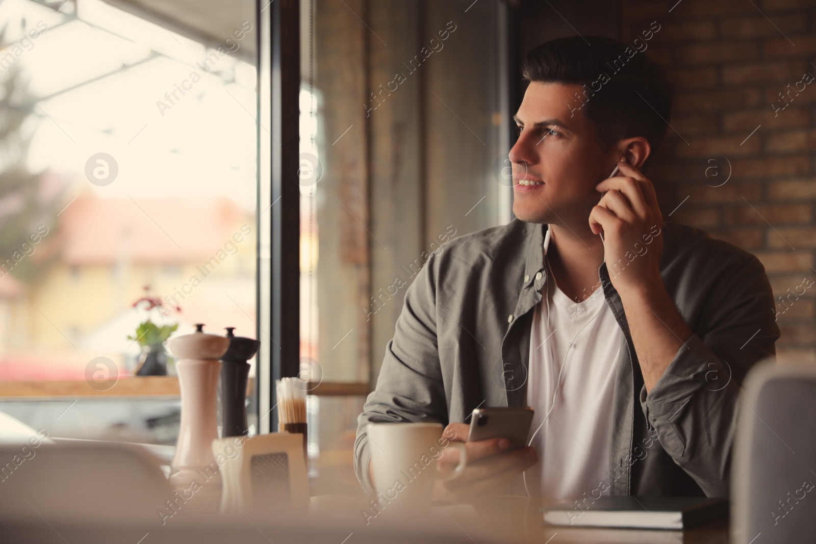 Photo of Man with smartphone listening to audiobook at table in cafe