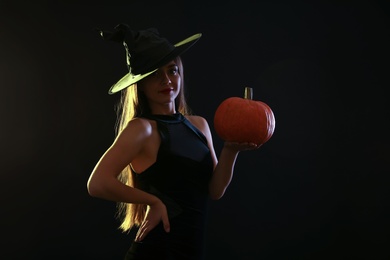 Young woman wearing witch costume with pumpkin on black background. Halloween party